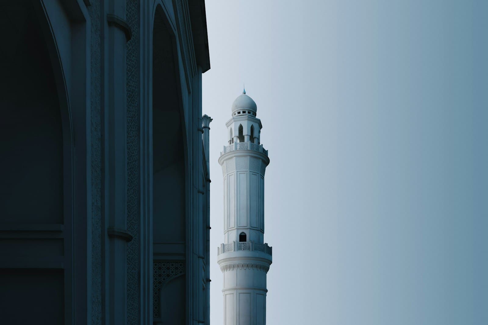 A white minaret standing tall beside an arched building