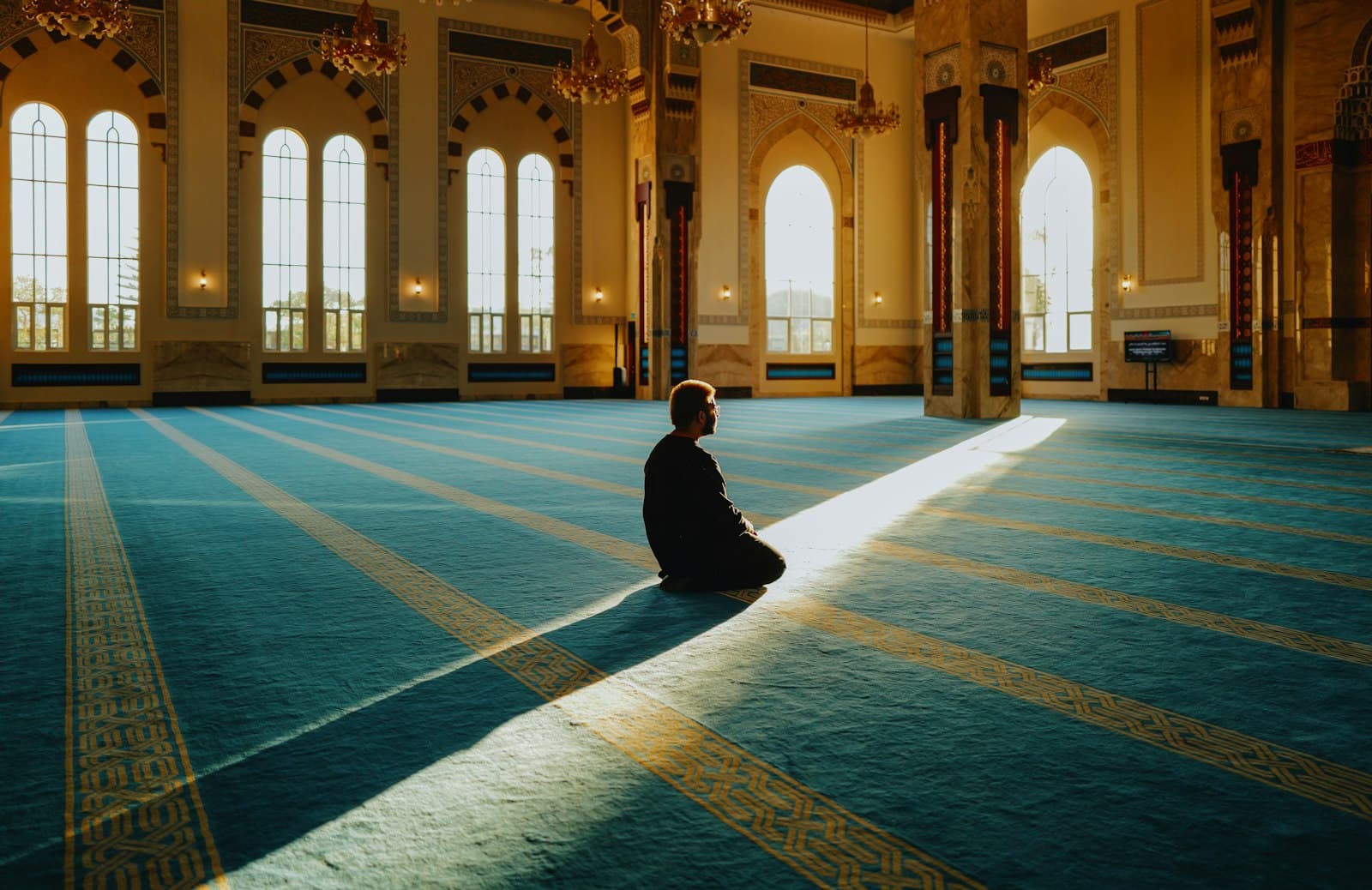 A man praying in a large, sunlit mosque