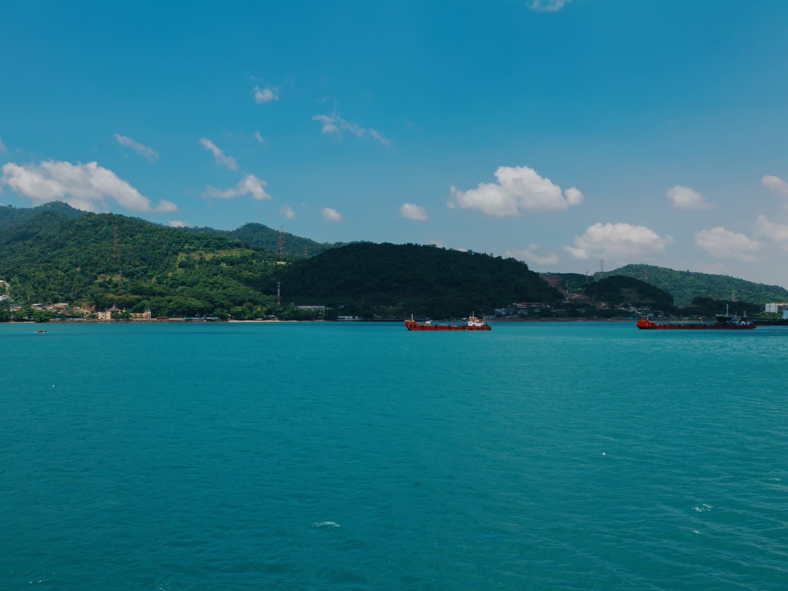 Cargo ships sailing on a bright blue sea near mountains